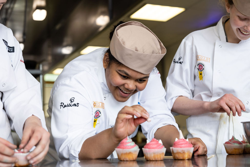 student chef smiling as she makes cupcakes
