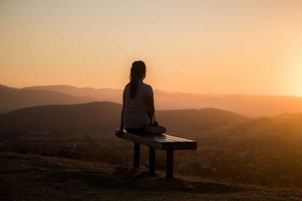 Lady sat on a park bench looking at the sunset.