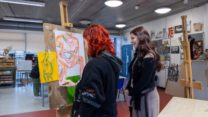 Art students painting on easels in a colourful studio.