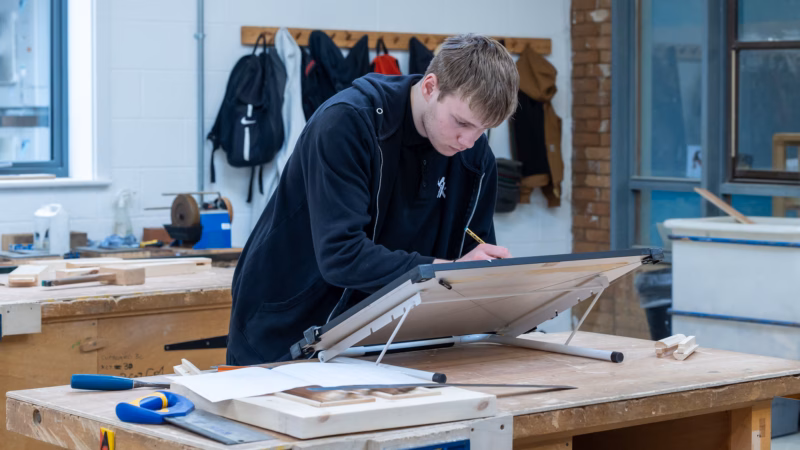 Construction students drawing technical plans at their workbenches.
