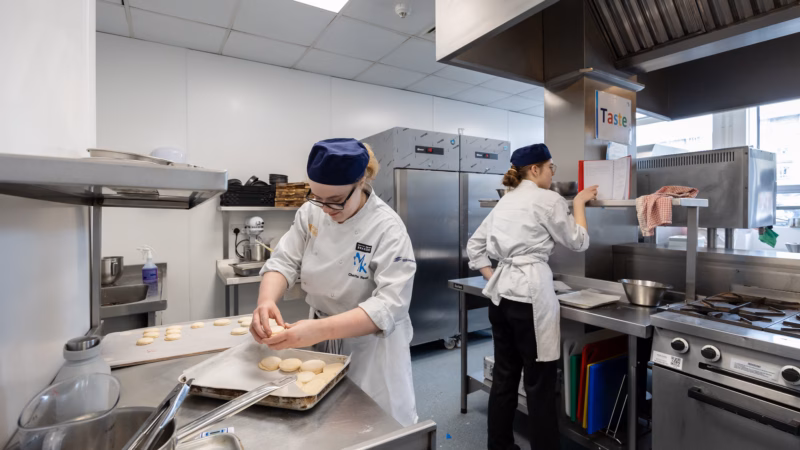 Professional chefs preparing dishes in a commercial training kitchen.