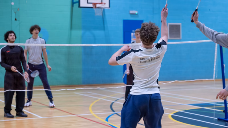 A student practising badminton in the college sports hall.