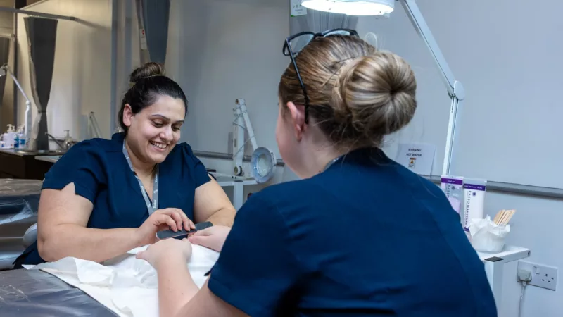 Nail technician student working on a client’s nails – A beauty student applying nail treatment in a salon setting.