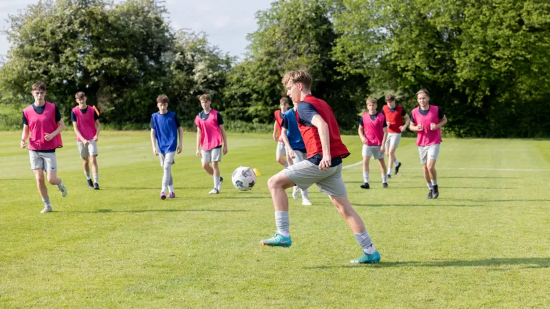Students playing football on a green field – Young athletes participating in an outdoor football match.