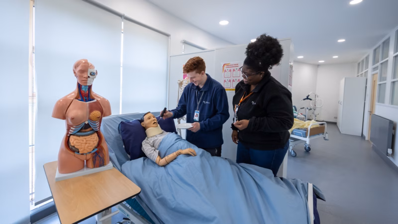 Health and social care students practising patient care with a hospital bed setup.
