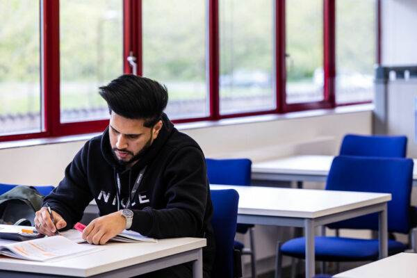 Student sat alone in a classroom writing in his textbook