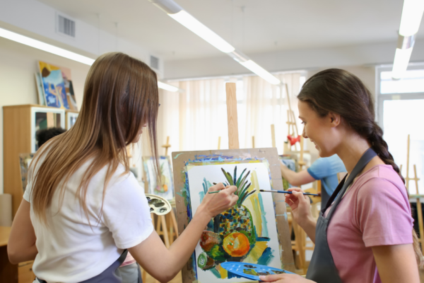 2 female art students painting a picture of fruit on an easel
