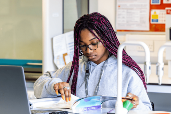 A young female MK College student, readying though a text book in a science lab.