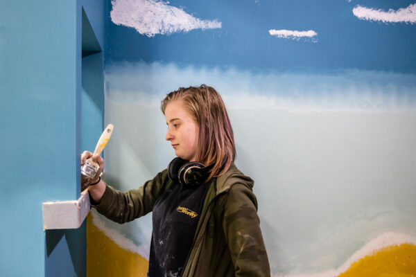 A female painting & decorating student, painting a beach scene on the wall