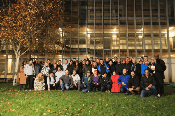 50 people from the Milton Keynes business community at the CEO Sleepout. Everyone is in outdoor clothes in the grassy area of MK College's Bletchley campus.