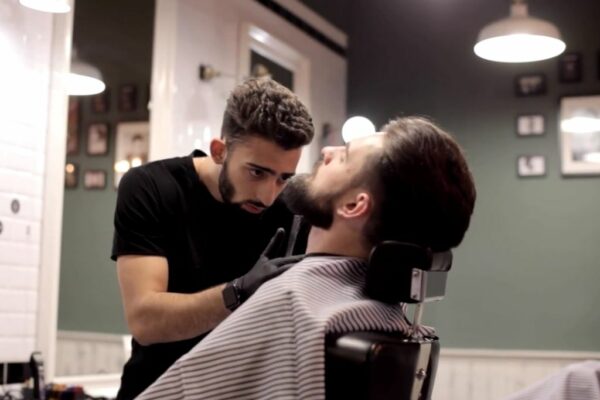 A man sitting in a barber's chair, getting his hair cut by a professional barber.