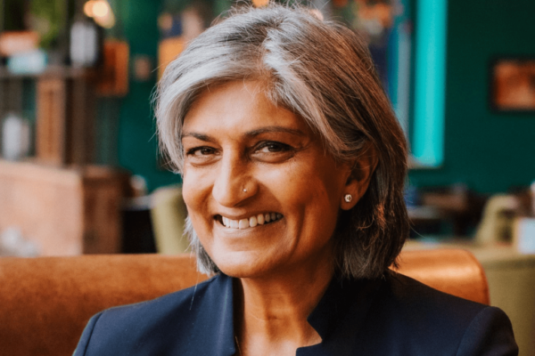 New Chair of Governors Ruby Parmar is facing the camera directly and smiling. Ruby is wearing a dark coloured suit and is in front of a green background.