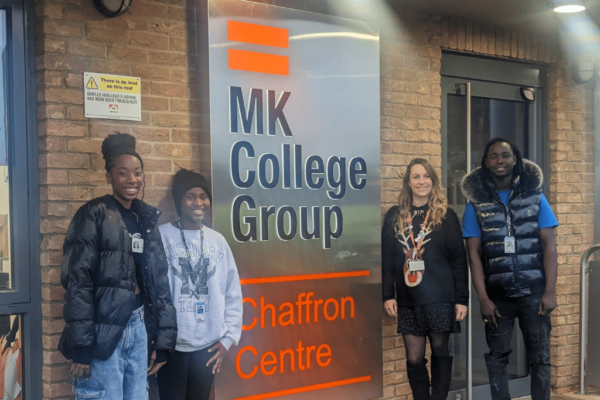 MK College's latest Student Commissioners for Racial Justice stood outside the College's Chaffron Way campus. Two students are stood to the left of the orange MK College Group sign and on the right is staff member Jessica Frohawk McLucas from the College with another Student Commissioner on the far left.