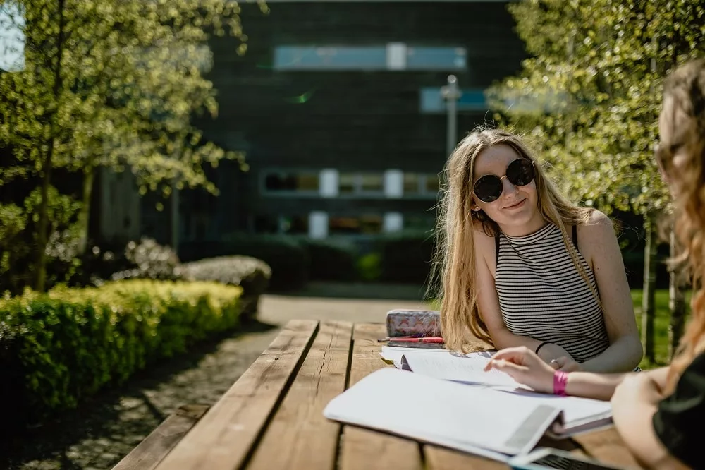 Students sat outside on a picnic bench working through textbooks