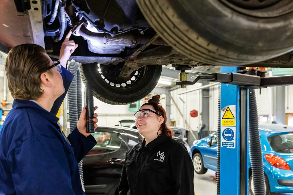 Motor vehicle students working on the underside of a car