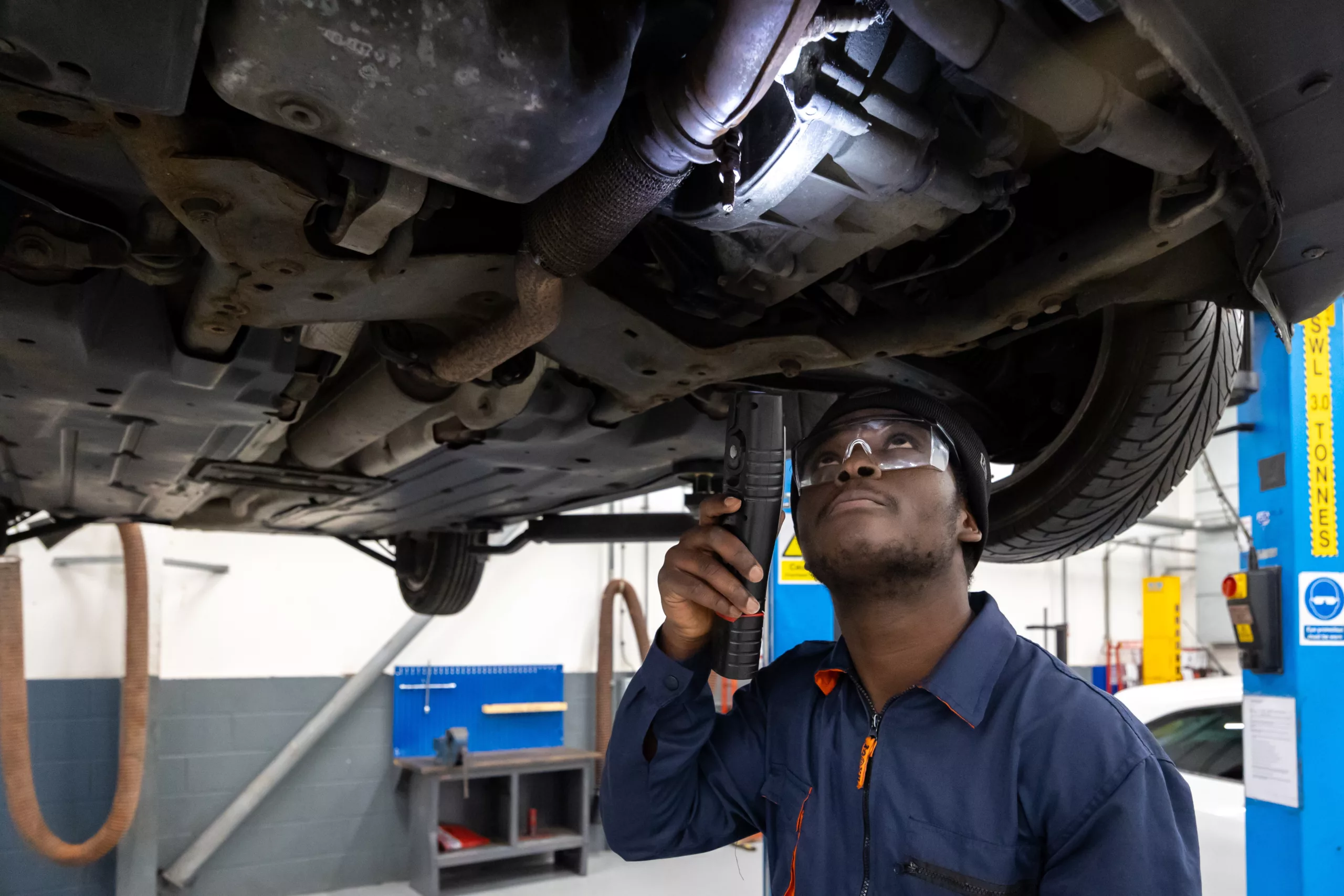 A mechanic inspecting the underside of a vehicle in a workshop.