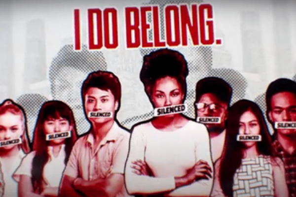 A still from a short film created by the Student Commission for Racial Justice. In the still, a group of young people are standing in a line with the word 'silenced' across their mouths. The words 'I do Belong' are above their heads in red letters.