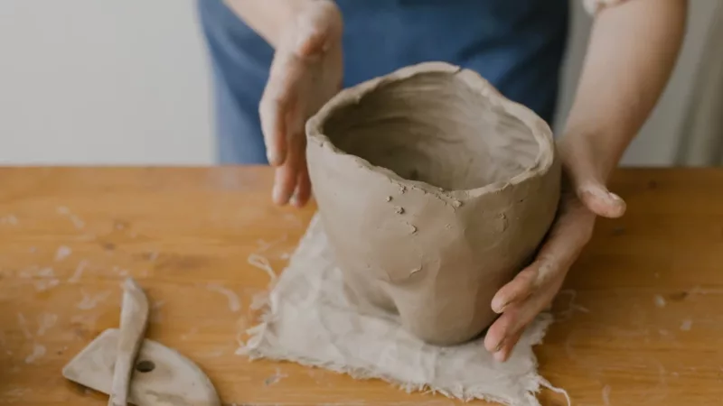 A picture of someone's hands working on a clay pot on a table.