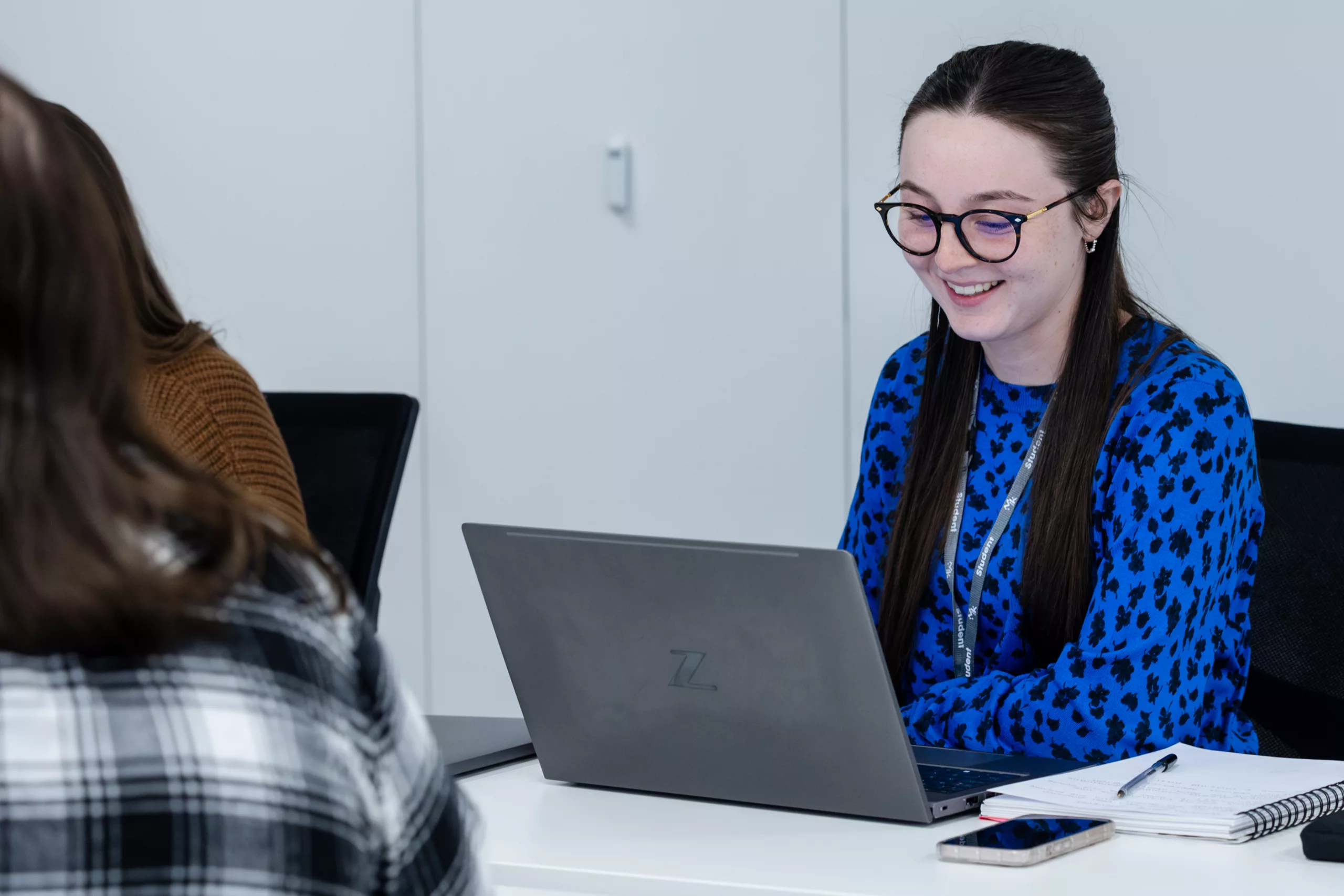 Student working on a laptop – A young woman wearing glasses and smiling while working on her laptop.