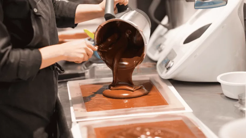 Chocolate tempering process – A person pouring melted chocolate into a mold during the chocolate-making process.