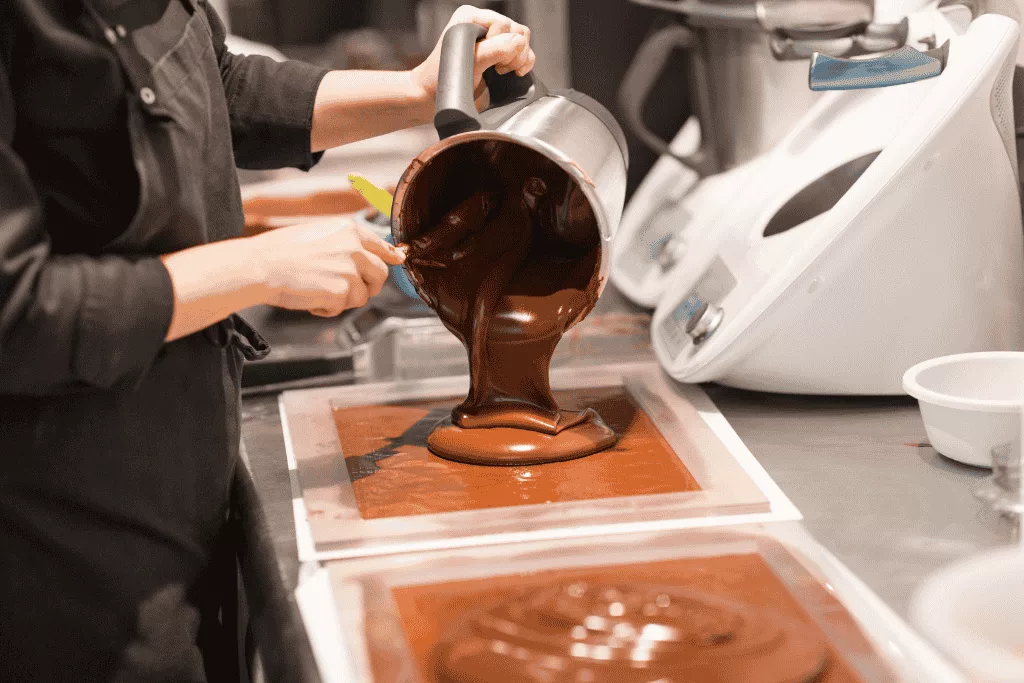 Chocolate tempering process – A person pouring melted chocolate into a mold during the chocolate-making process.