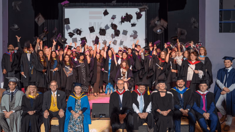 Students from Milton Keynes College and the South Central Institute of Technology at the 2025 graduation ceremony. The students are throwing their graduation caps into the air and smiling.