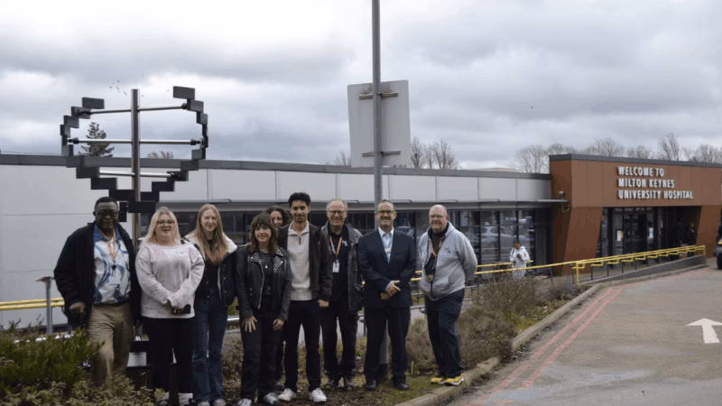 MK College and students and staff stood in a row in front of a spiral sculpture outside of Milton Keynes University Hospital.